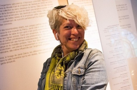 Image of Mar Dixon, from the waist up. She is smiling and casually dressed, wearing a denim jacket, scarf, and earbuds.