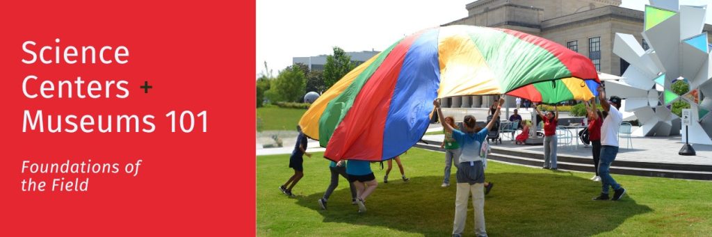 A group of people holds up a large, colored play parachute on a lawn in front of a museum. Text reads "Science Centers + Museums 101: Foundations of the Field"