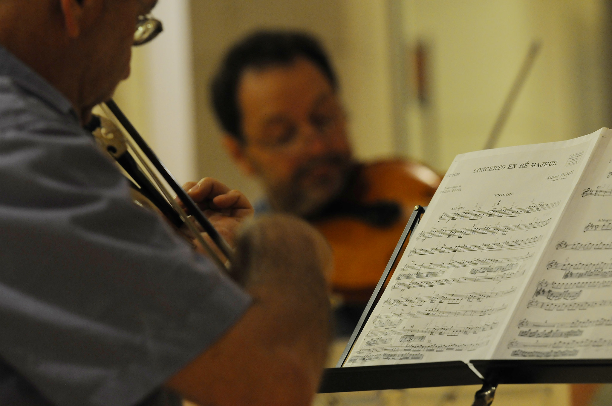 Man wearing glasses playing the violin and looking down at a sheet of music.